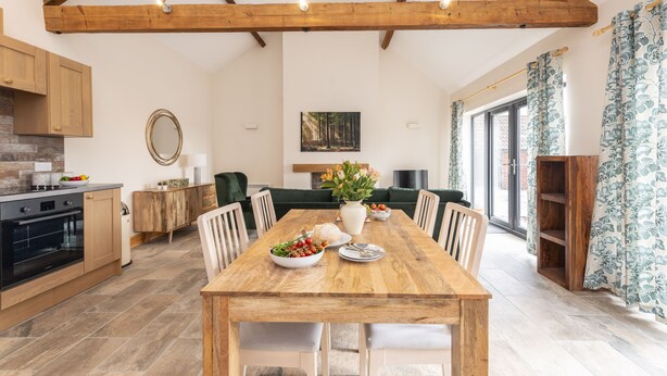 A spacious dining area with a wooden table and chairs, a kitchen with modern appliances, and a large window with curtains. - A marketing that sleeps 2 guests  in 1 bedroom (Trowbridge)