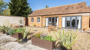 A brick house with a tiled roof, a patio with wooden furniture, and potted plants. - A marketing that sleeps 2 guests  in 1 bedroom (Trowbridge)