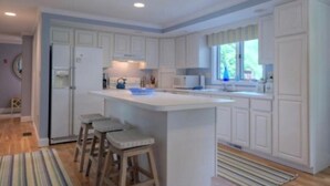 A modern kitchen with white cabinetry, a central island with stools, and a large window providing natural light. - Jenness Beach Ocean Getaway - Book Now for Summer '26! (Rye)