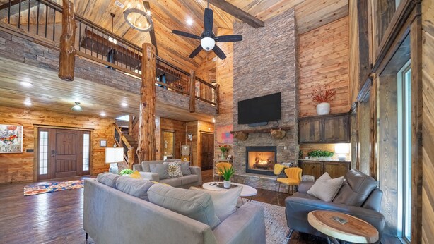 A spacious living area with a fireplace, high ceilings, and a wooden interior. - Great family cabin! Huge deck! Creek! Mini cabin! Lots of amenities! (Hochatown)