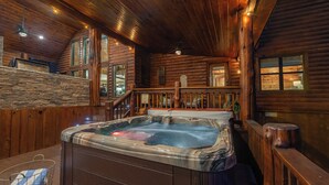 A wooden cabin interior with a hot tub, stone wall, wooden staircase, and a view of the outdoors. - Great family cabin! Huge deck! Creek! Mini cabin! Lots of amenities! (Hochatown)