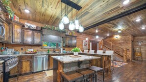 A rustic kitchen with wooden cabinets, a central island with stools, and a wooden staircase leading to another level. - Great family cabin! Huge deck! Creek! Mini cabin! Lots of amenities! (Hochatown)