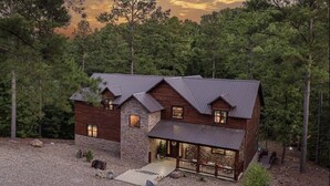 A log cabin with a stone foundation, multiple chimneys, and a porch with outdoor seating. - Great family cabin! Huge deck! Creek! Mini cabin! Lots of amenities! (Hochatown)