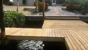 Una terraza de madera que conduce a una piscina, con una casa al fondo.