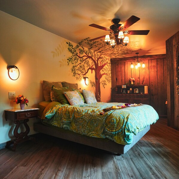 A bedroom with a bed, a ceiling fan, a nightstand, a wall-mounted lamp, and a wooden dresser. - Unique Treehouse With Spectacular View. (Springfield)