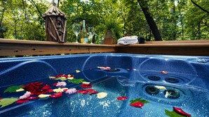 Ein Whirlpool mit Rosenblättern und einer Holzkonstruktion in bewaldeter Landschaft.