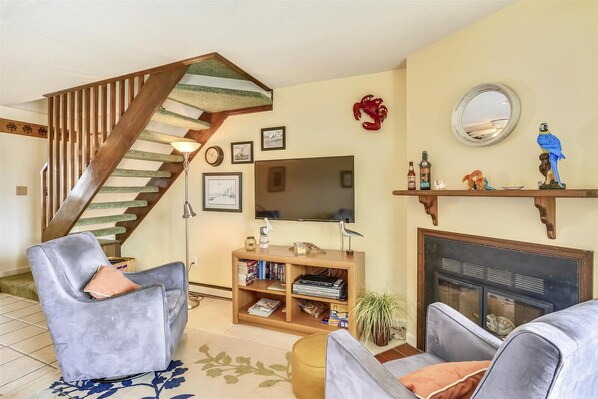A living room with a staircase, a fireplace, a television, and a bookshelf.