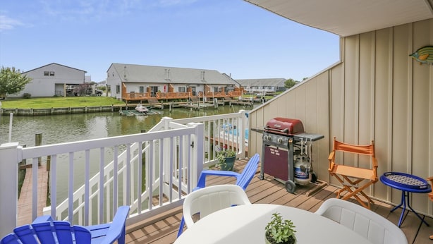 A deck with outdoor seating, a grill, and a view of a canal with houses in the background. - Canal - Waterfront, WIFI, Walking Distance to Boardwalk / Beach Discount 6-27-26 (Ocean City)