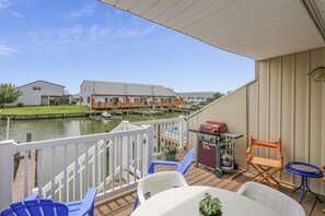 A deck with outdoor seating, a grill, and a view of a canal with houses in the background.