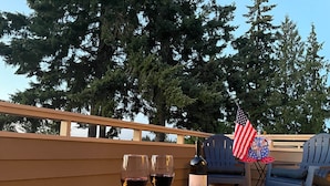 A terrace with a fire feature, two glasses of red wine, a bottle of wine, and an American flag. - Oceanview | Big Deck | Modern Home - Crash Pad BnB (Port Angeles)