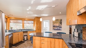 A modern kitchen with wooden cabinets, a granite countertop, and a built-in dishwasher. - Oceanview | Big Deck | Modern Home - Crash Pad BnB (Port Angeles)