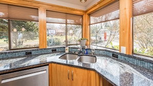 A kitchen with a double sink, wooden cabinets, and a view of the outdoors. - Oceanview | Big Deck | Modern Home - Crash Pad BnB (Port Angeles)