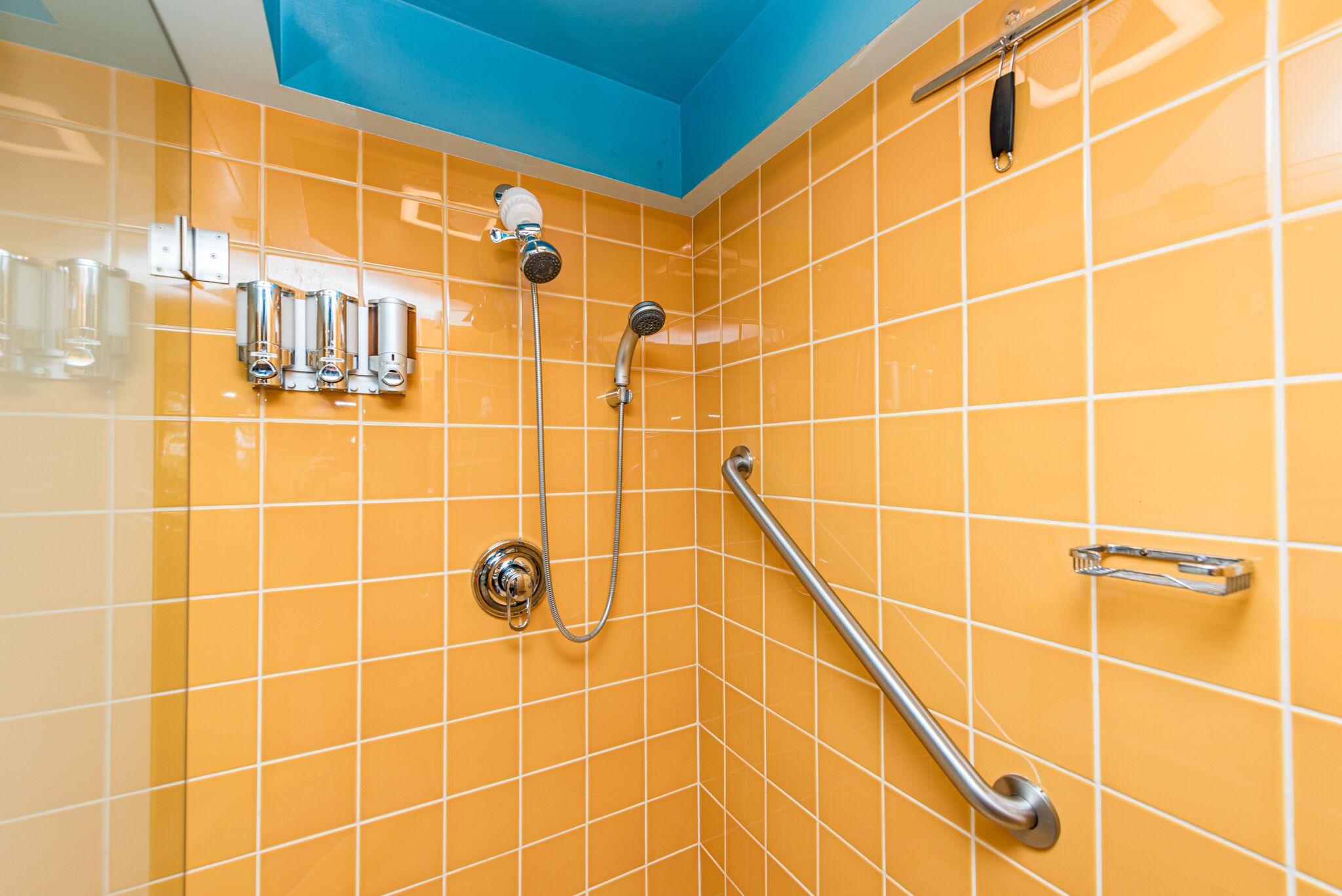 A bathroom with orange tiles, a blue ceiling, and a handrail.