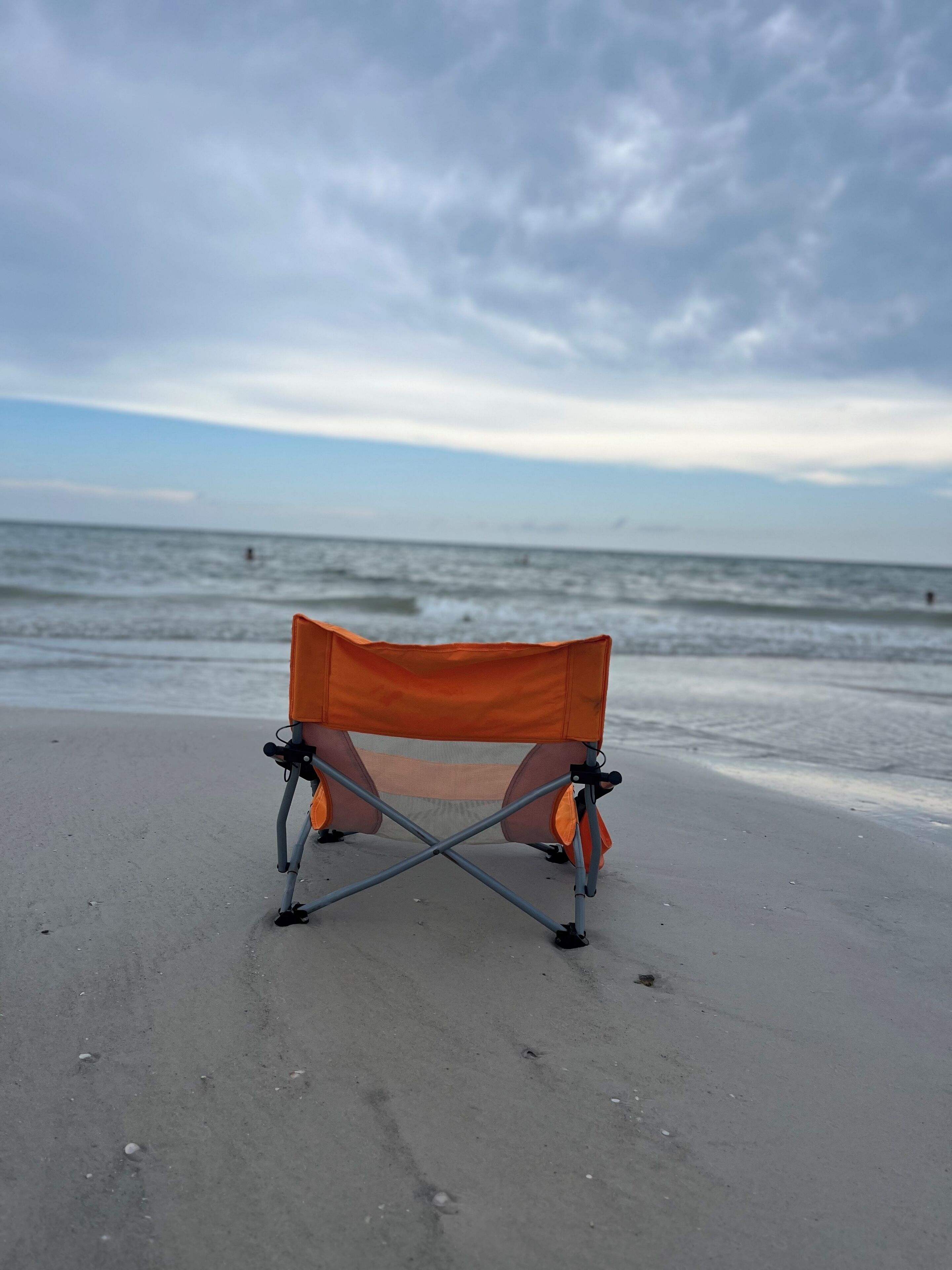 A beach with a single orange camping chair.