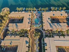 Vista aérea de un resort con una piscina central, varias zonas de estacionamiento y palmeras.