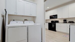 A compact kitchen with white cabinets, a microwave, a stove, and a washing machine.