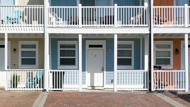 A multi-story residential building with a central door, balconies, and a brick driveway.
