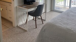 A bedroom with a bed, a desk with a chair, a television, a bathroom with a sink, and a balcony with a railing.