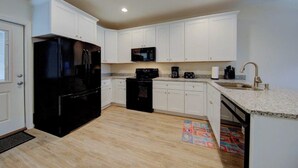 A compact kitchen with white cabinets, a black refrigerator, a microwave, a coffee maker, and a sink.