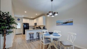 A modern kitchen with white cabinets, a central island, and a dining area with a round table and chairs.
