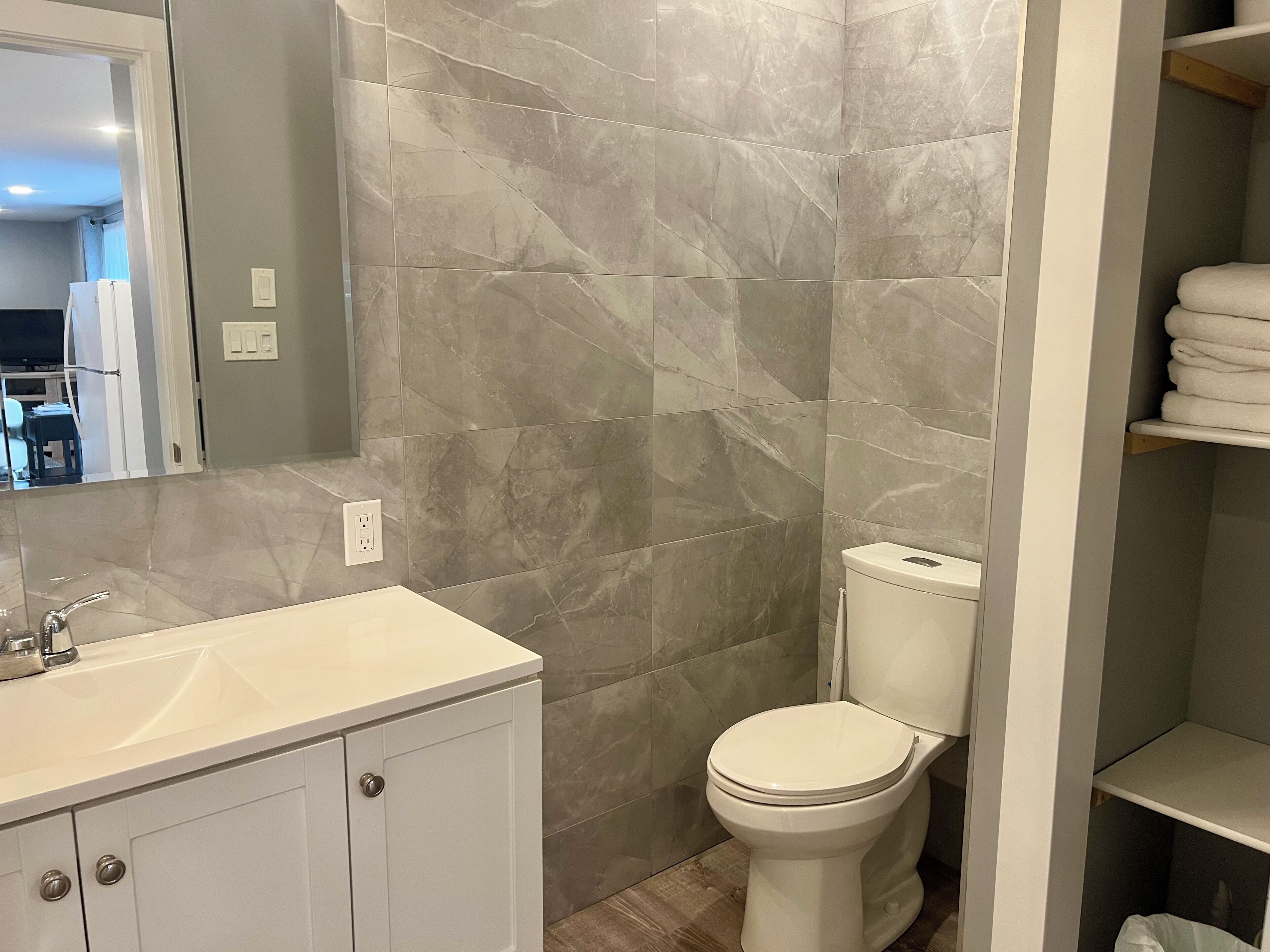 Een badkamer met een wit wastafelmeubel, een toilet en muren met een marmerprint.