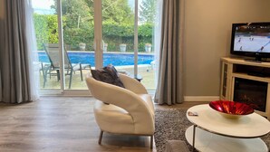 A living room with a beige leather sofa, a glass door leading to a pool, and a television on a stand.