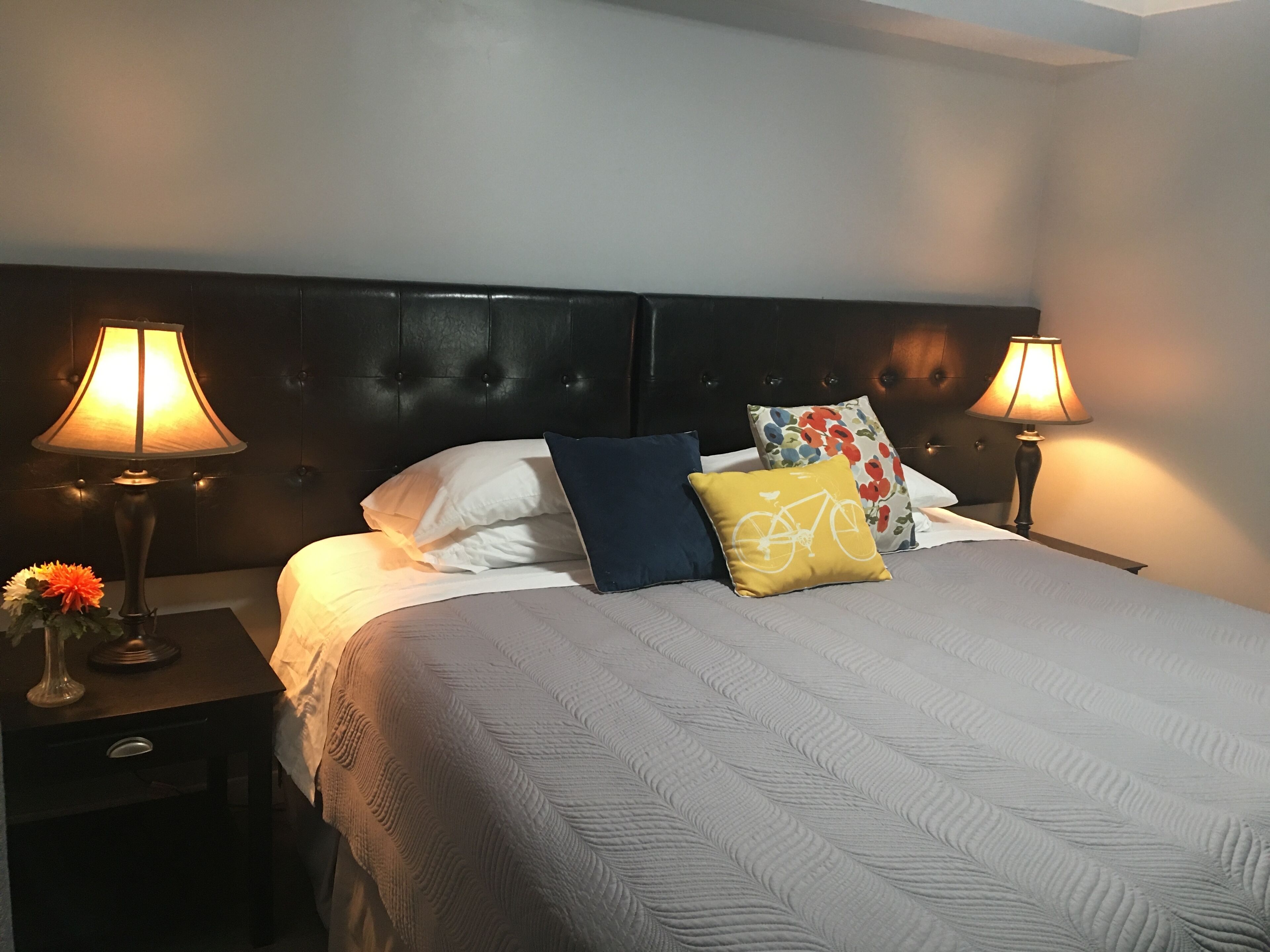A neatly made bed with a patterned bedspread, two bedside lamps, and a nightstand with a vase of flowers.