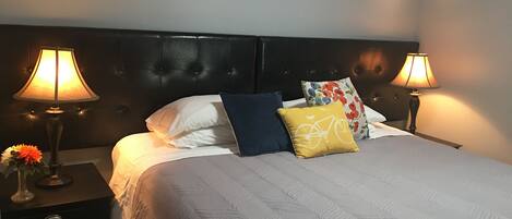 A neatly made bed with a patterned bedspread, two bedside lamps, and a nightstand with a vase of flowers.