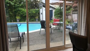 A sliding glass door leading to a patio with a pool, outdoor furniture, and a view of a backyard with greenery.