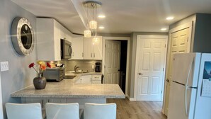 A modern kitchen with a granite countertop, white bar stools, a built-in oven, and a refrigerator.