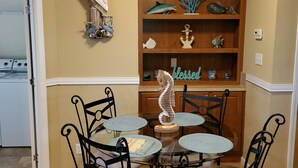 Een eetruimte met een ronde tafel en vier stoelen, een houten boekenkast met decoratieve objecten, en een wandlamp.
