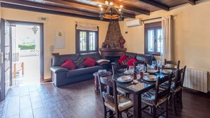 A dining area with a table set for four, a sofa with red cushions, and a stone fireplace. - La Casita de Ronda by Ruralidays (Málaga)