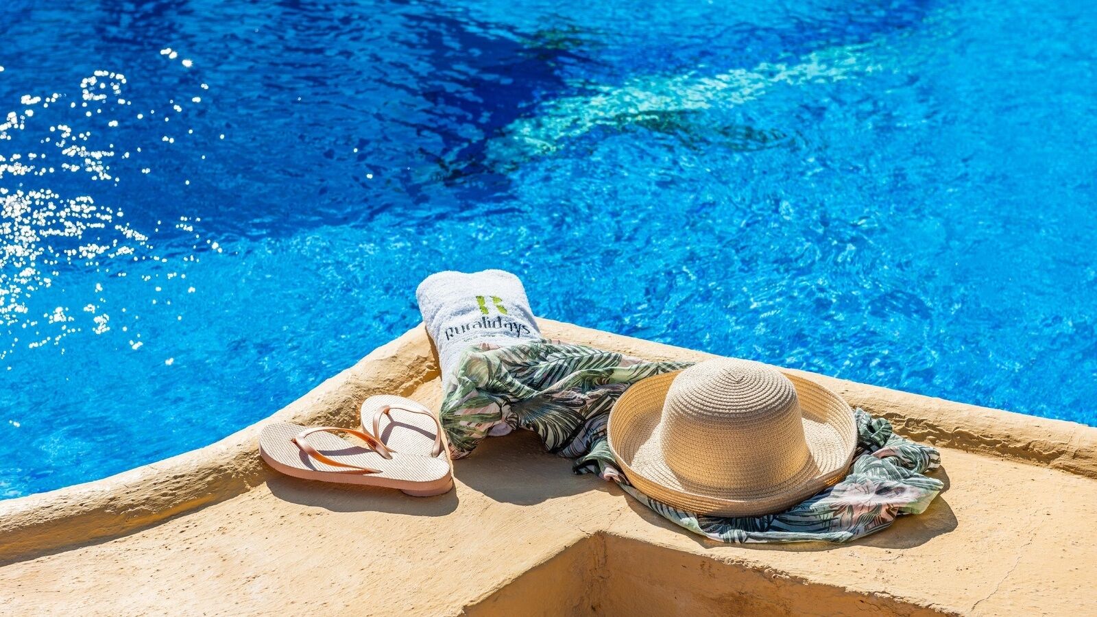 Ett område vid poolen med en handduk, en hatt och sandaler.