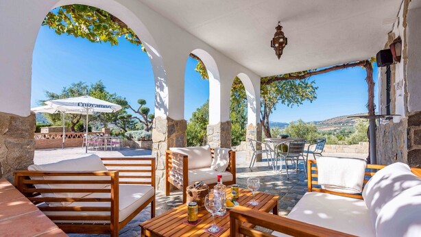 An outdoor seating area with stone pillars, wooden furniture, and a view of the landscape. - La Casita de Ronda by Ruralidays (Málaga)