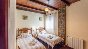 A bedroom with two beds, a stone wall, a wooden ceiling, and a radiator. - La Casita de Ronda by Ruralidays (Málaga)