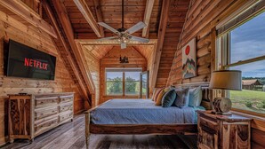Un dormitorio de cabaña de madera con cama, cómoda de madera, televisor y vistas al exterior.