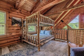 Interior rústico de uma cabana de madeira, com uma cama de quatro andares, uma janela grande e vista para o exterior.