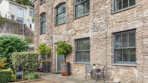 A stone building with multiple windows and a small patio area with a table and chairs.