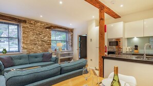 A cozy living room with a blue sofa, a dining table set with plates and wine glasses, and a kitchen area with modern appliances.