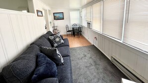 A compact living space with a grey sofa, a small dining table, and a view of the outdoors through large windows with blinds. - Avalon BEACH BLOCK with a POOL: 1 Bedroom (Avalon)