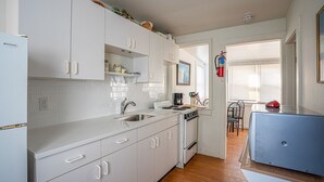 A kitchen with white cabinets, a stove, and a sink. There is a window with blinds and a door leading to another room. - Avalon BEACH BLOCK with a POOL: 1 Bedroom (Avalon)