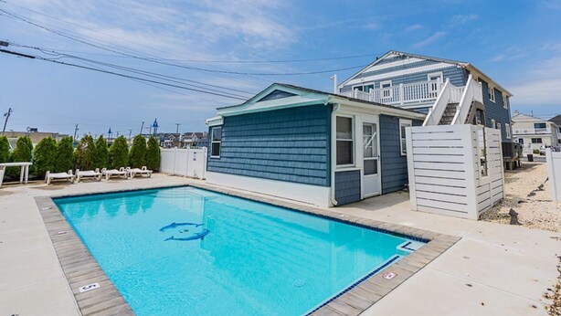 A swimming pool with a blue deck, a small building with a white roof, and a staircase leading to a house with a blue exterior. - Avalon BEACH BLOCK with a POOL: 1 Bedroom (Avalon)