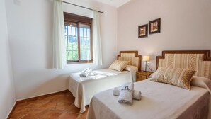 Ein Hotelzimmer mit zwei Betten, einem Fenster mit Vorhängen, einem Nachttisch mit Lampe und zwei gerahmten Bildern an der Wand.