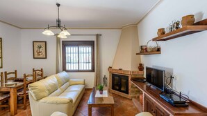 Ein Wohnzimmer mit einer Couch, einem Esstisch, Stühlen, einem Kamin, einem Fernseher und Regalen mit Dekoration.