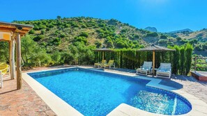 Ein Pool mit Liegestühlen und einer Pergola, umgeben von viel Grün und Hügeln.
