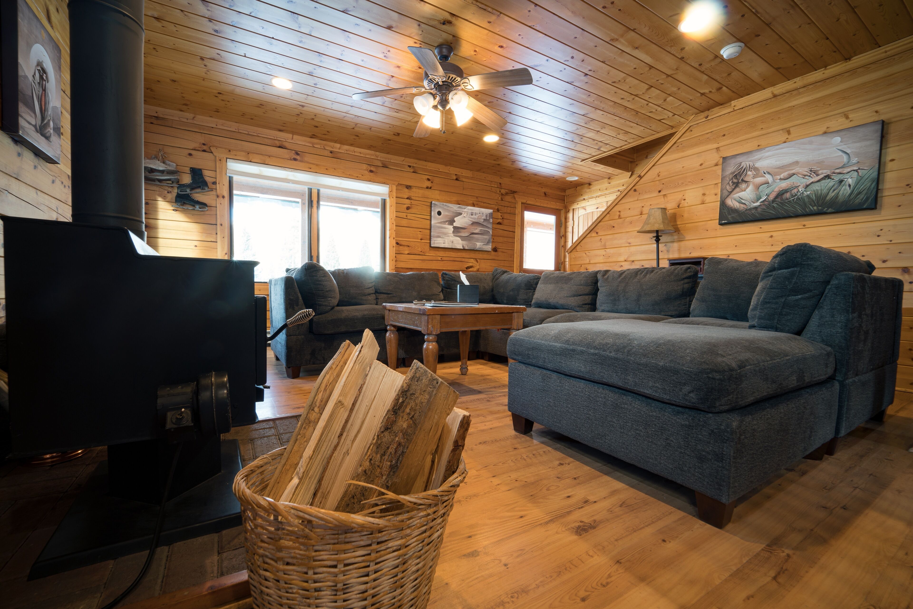 A cozy cabin interior with a fireplace, wooden walls, a sofa, and a ceiling fan.
