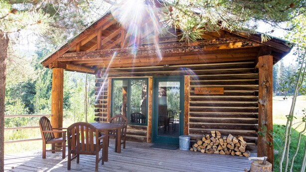 A wooden cabin with a deck, a table, and chairs. - Beyul Retreat (Meredith)