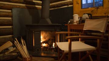 A cozy cabin interior with a wood-burning stove, a chair, and a window overlooking a forest.