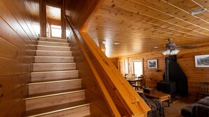 A wooden interior with a staircase, a ceiling fan, a fireplace, and a dining area. - Beyul Retreat (Meredith)