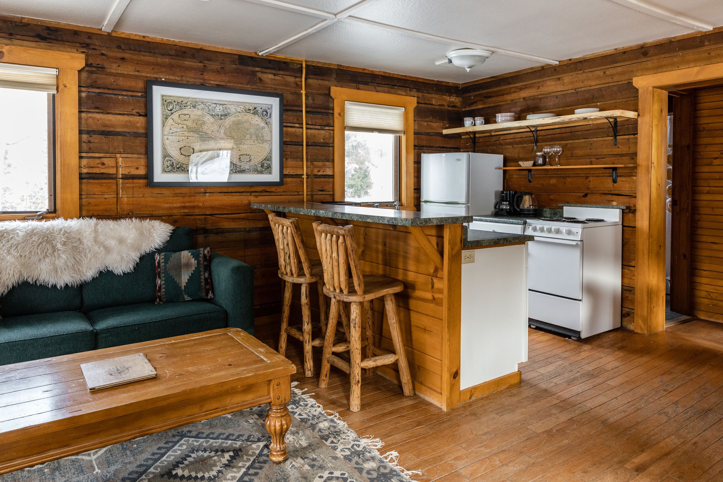 Cocina estilo cabaña acogedora, con paredes de madera, una isla central con taburetes de bar, un refrigerador blanco y una estufa.